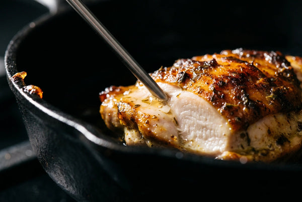 Sonde de cuisine plantée dans un haut de cuisse de poulet mariné poêlé, chair blanche et opaque, croûte caramélisée